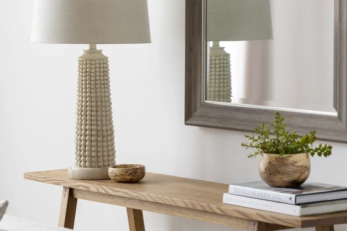 cream table lamp on an accent table with books & a mirror 