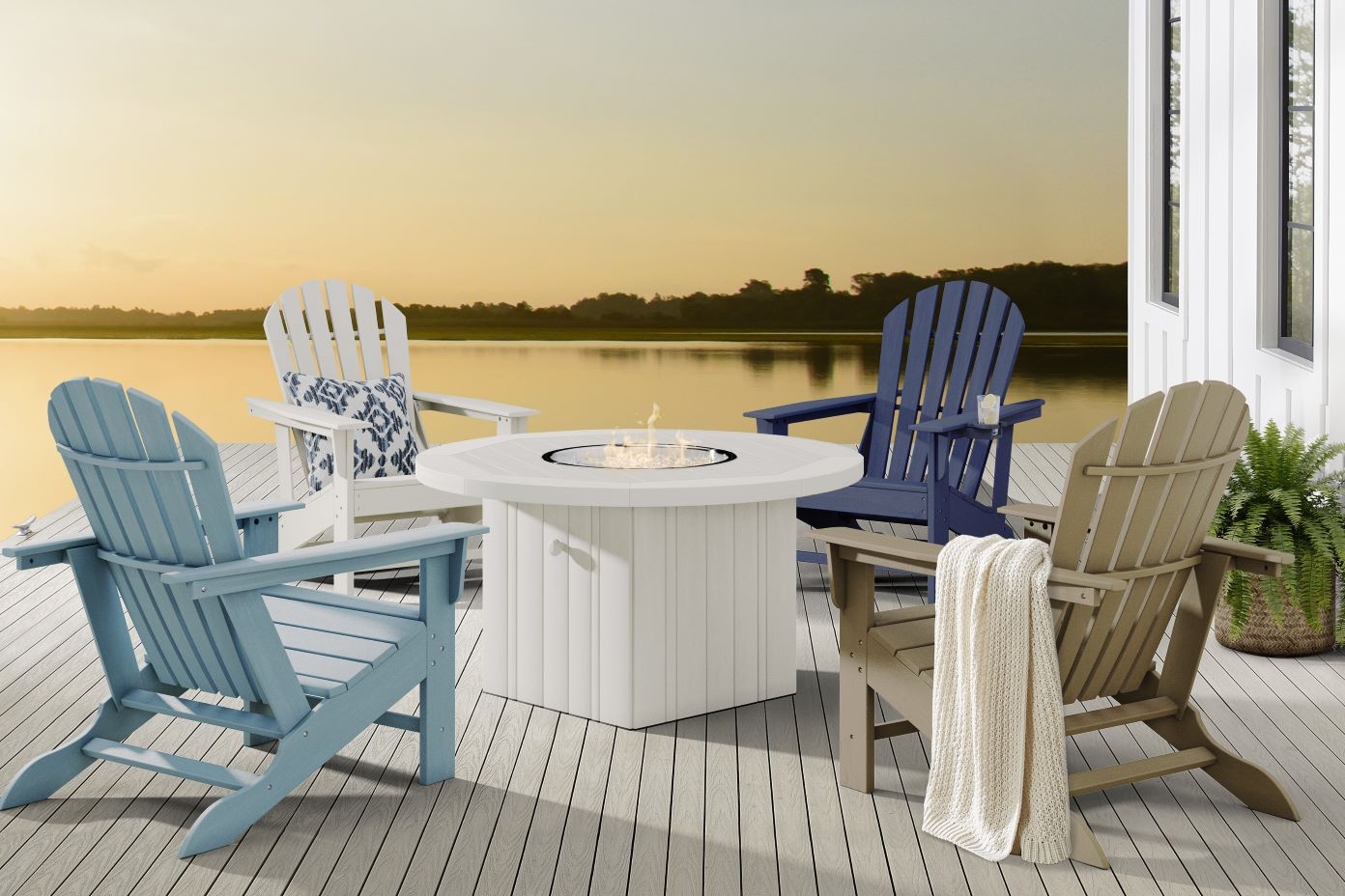Four Adirondack chairs around a white fire pit on a deck overlooking a lake.
