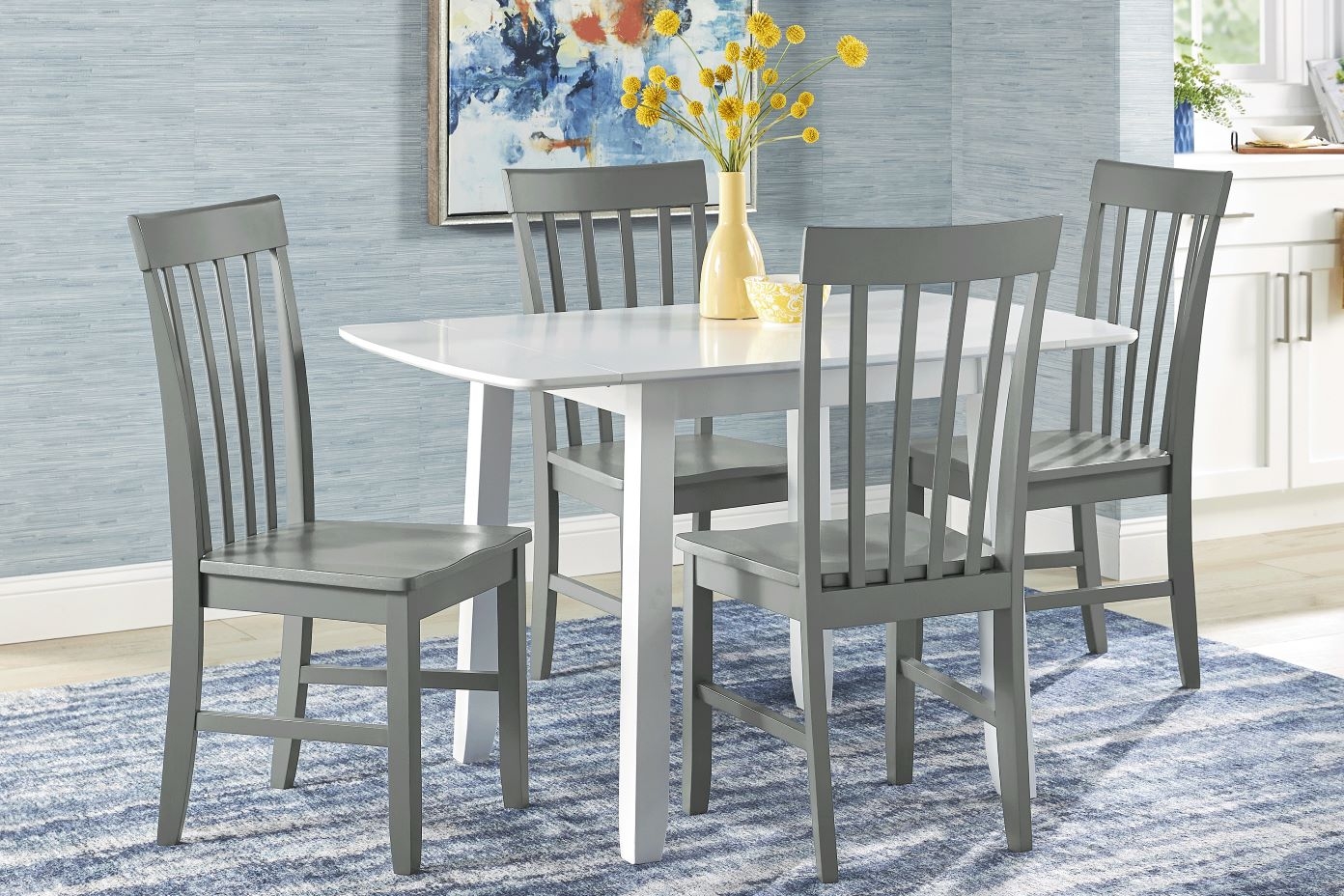 A white and gray dining table with four gray chairs on a blue rug.
