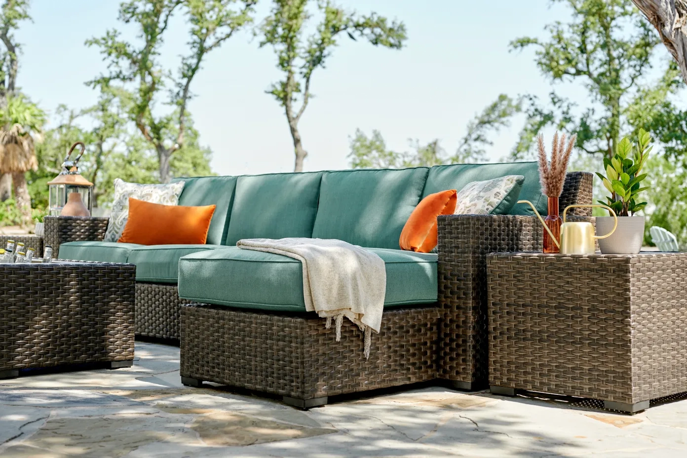 Outdoor wicker sofa with green cushions, orange pillows, and cozy throw blanket