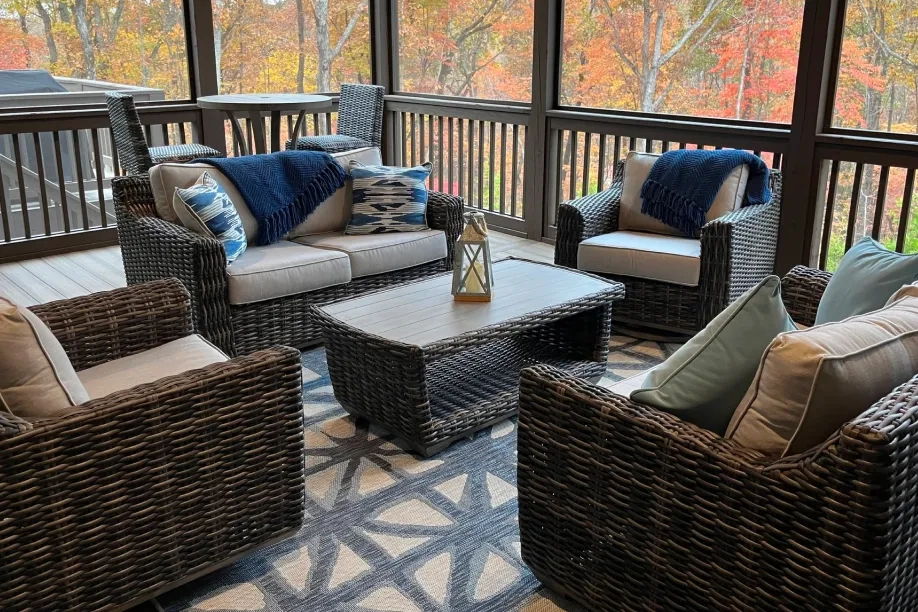 Cozy screened-in porch with wicker furniture, blue accents, and a fall foliage view