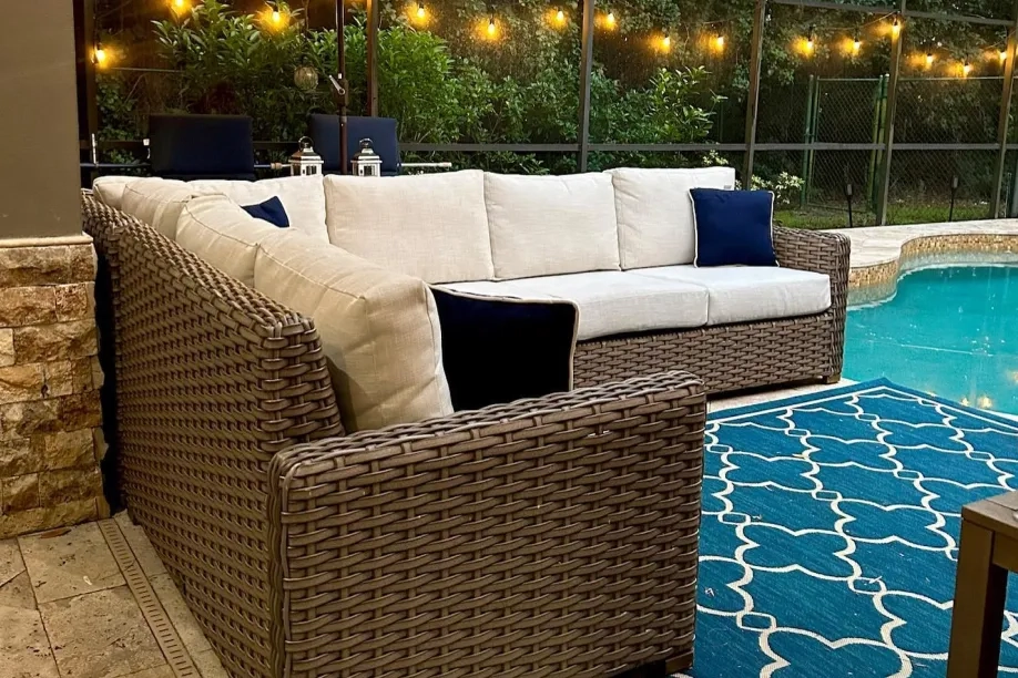 Wicker outdoor sectional with white cushions on a blue pattern rug