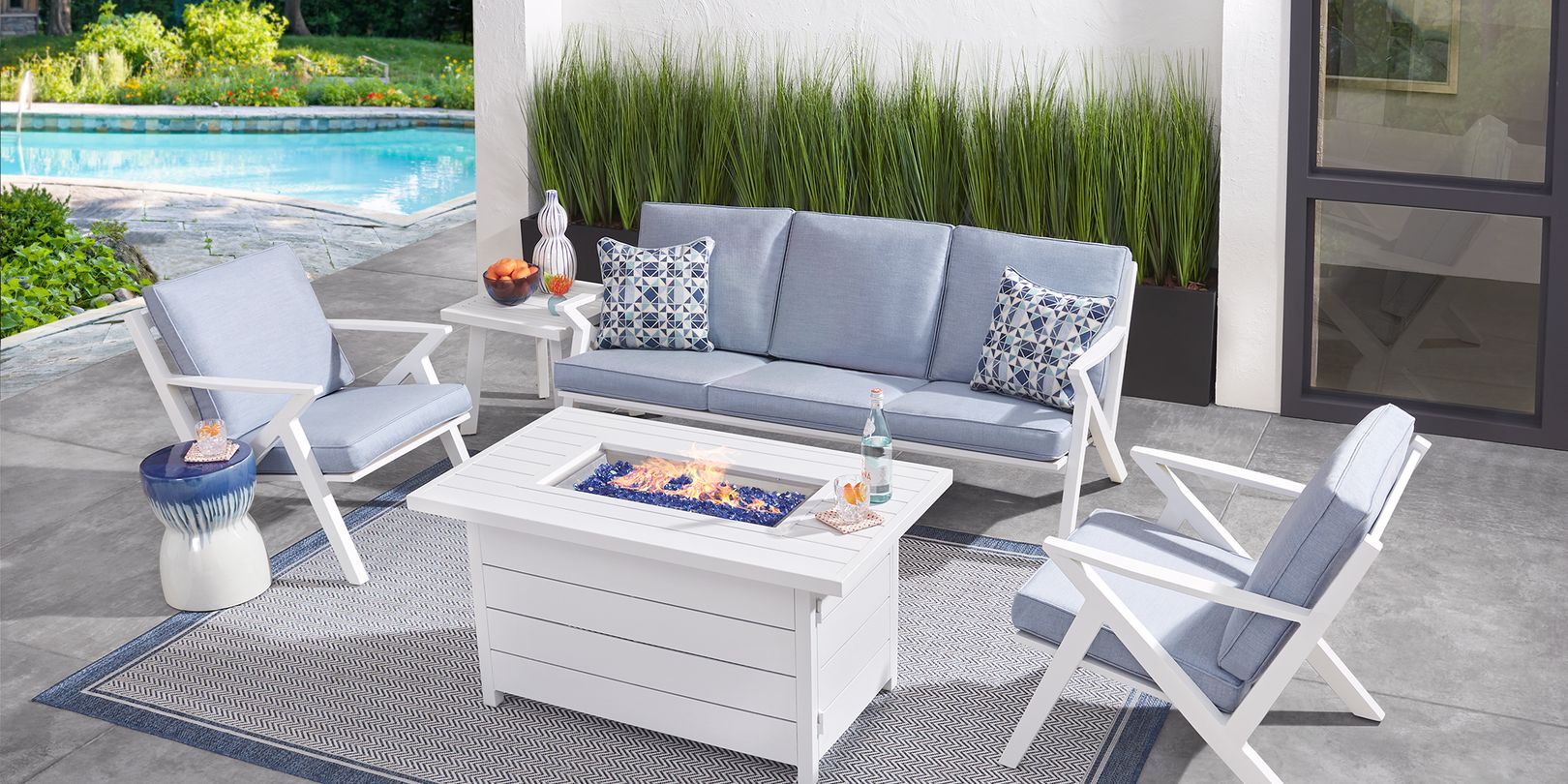 Photo of a white patio seating set with blue cushions and a fire pit table