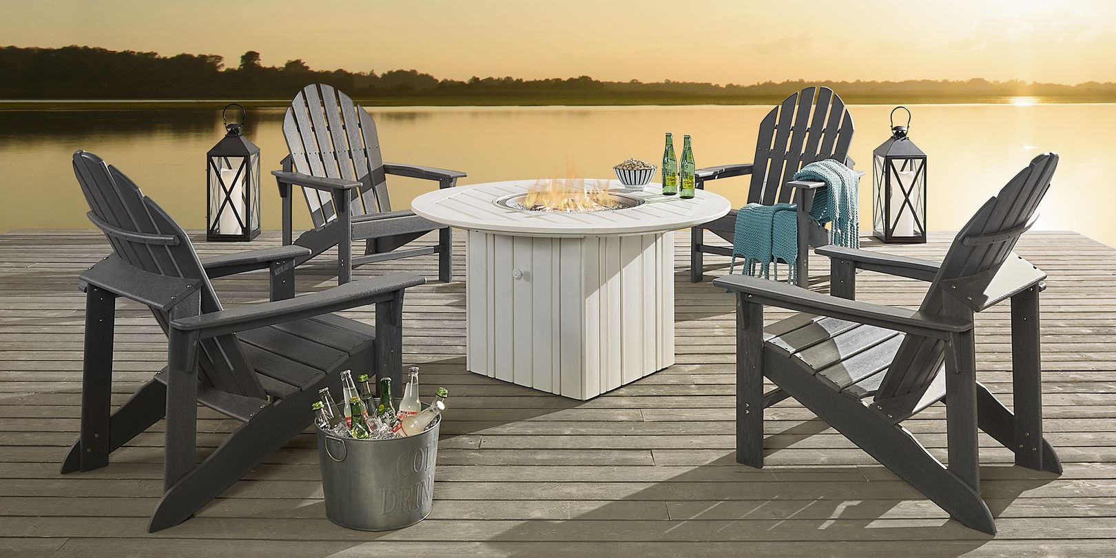 photo of 4 gray Adirondack chairs around  white fire pit table on a deck with lanterns placed at the edges