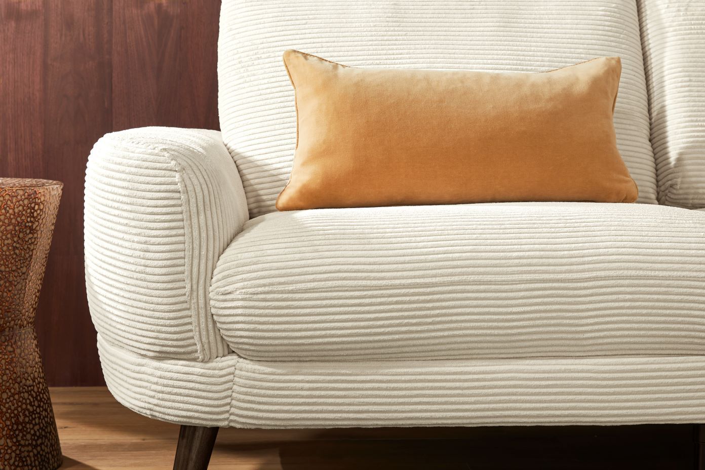 Cream corduroy armchair with an orange pillow.
