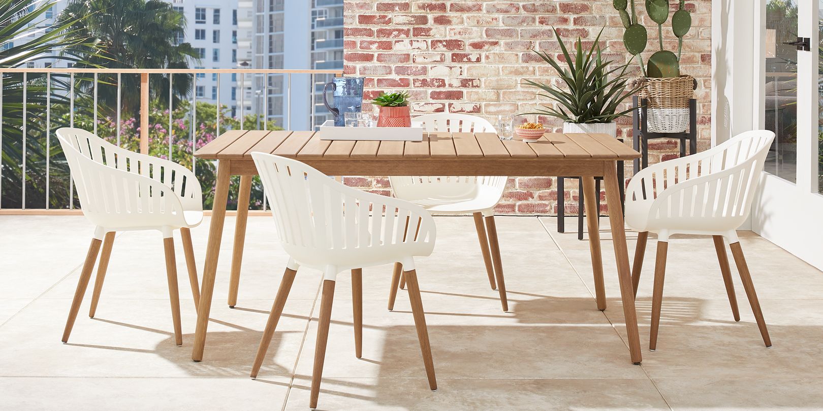 Photo of white and teak patio dining set on a balcony with a brick wall and plants in wicker baskets