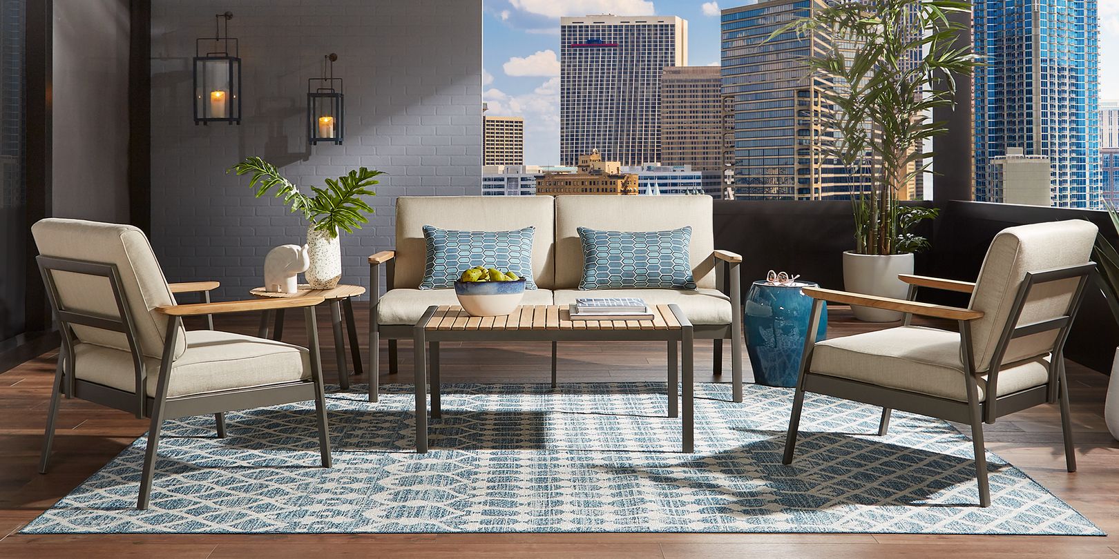 Photo of teak and metal patio seating set with tan cushions on a balcony with wall sconces