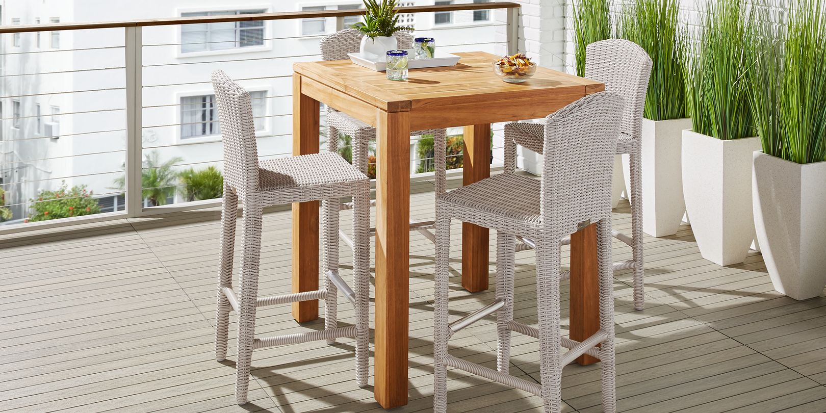 Photo of teak bar height table and white wicker stools on a balcony