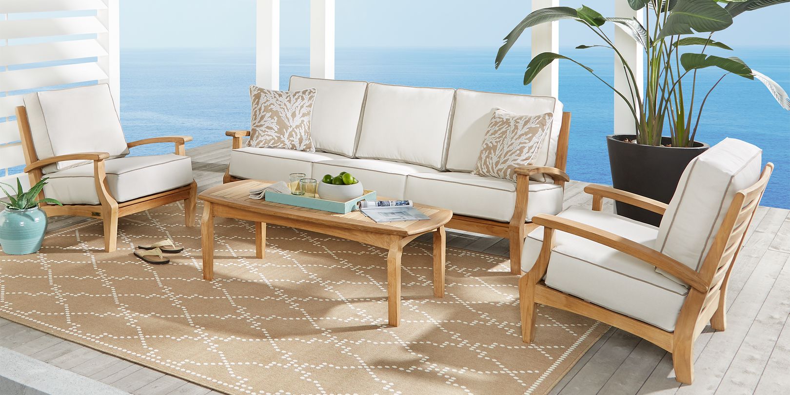Photo of a coastal teak patio seating set with tan cushions, a beige rug and coral print cushions
