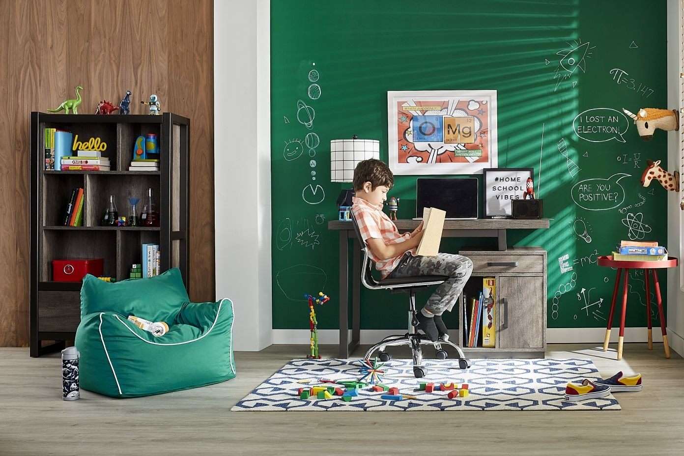 A boy reading at a desk in a room with a green chalkboard wall.
