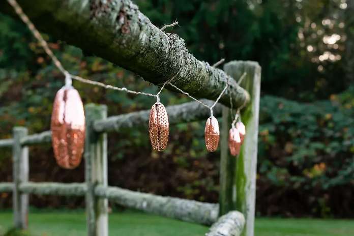 String lights with copper-colored acorn-shaped covers hanging on a wooden fence.
