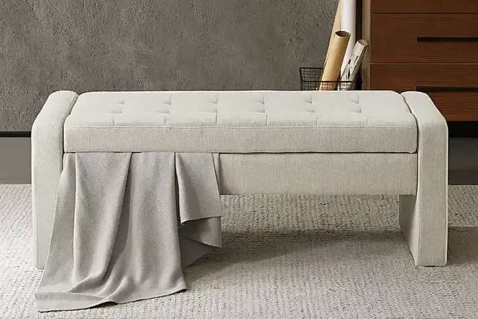 Beige upholstered storage bench with a blanket draped over it.
