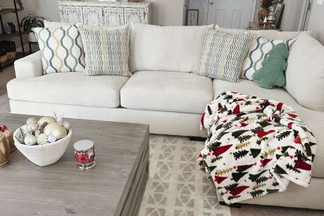 A cream-colored sectional sofa with decorative pillows and a Christmas tree blanket.
