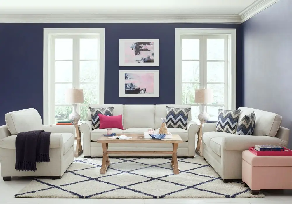 A living room set with a beige sofa, loveseat, and armchair, arranged around a wooden coffee table on a patterned rug.