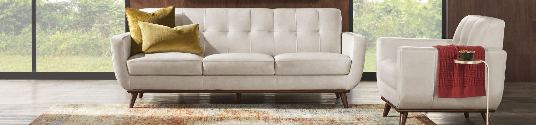 Cream-colored sofa and armchair with wooden legs, two yellow pillows, and a red throw.
