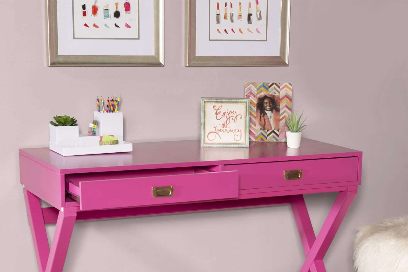 Pink desk with open drawer, framed art, and desk accessories.
