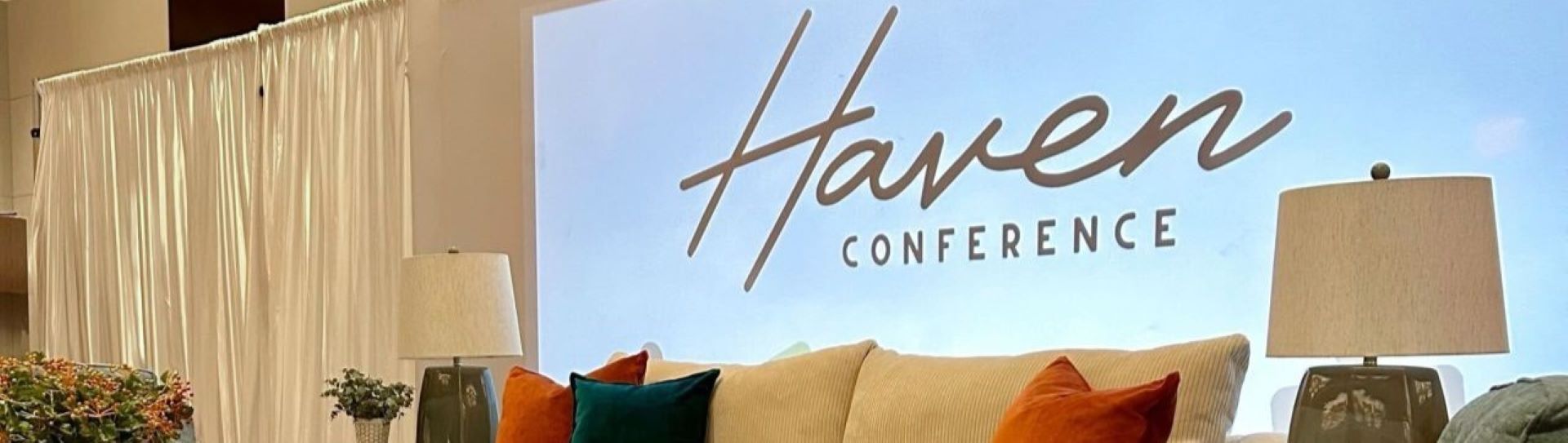 Haven CONFERENCE. A couch with pillows and lamps in front of a screen.