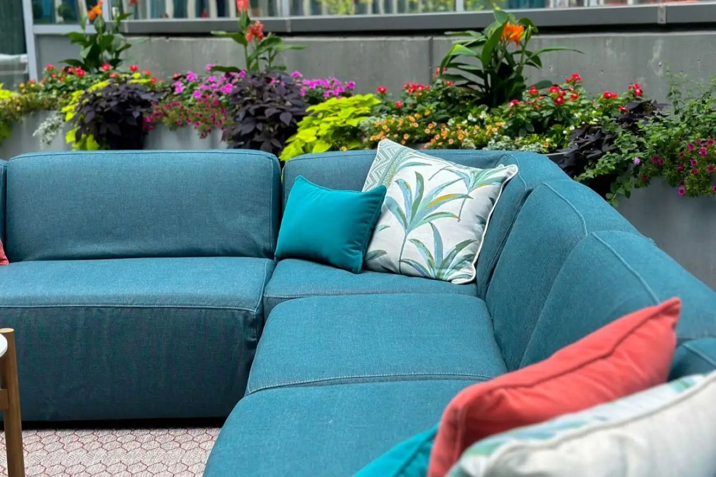 Teal sectional sofa with colorful pillows and flowers in the background.
