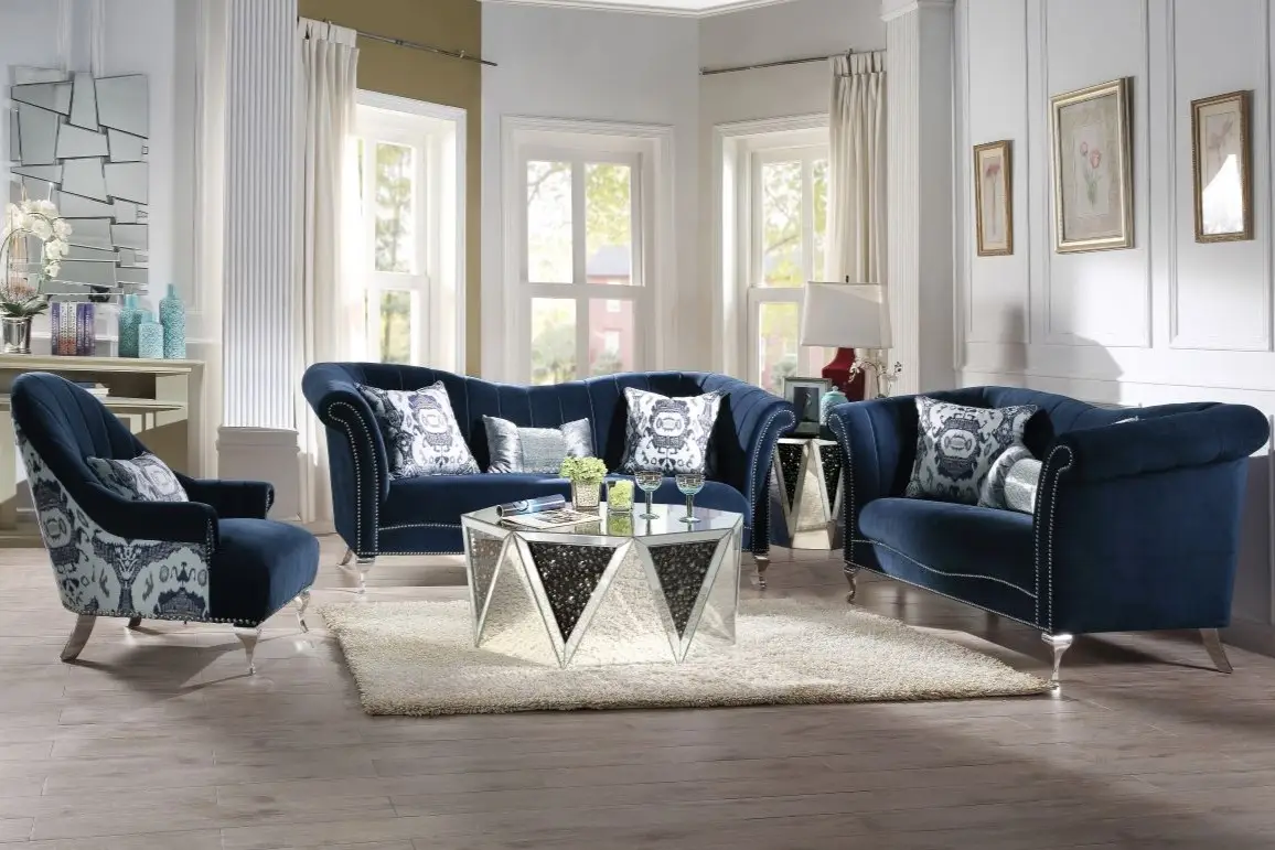 A living room set featuring a navy blue velvet sofa, loveseat, and armchair with silver accents and a mirrored coffee table.
