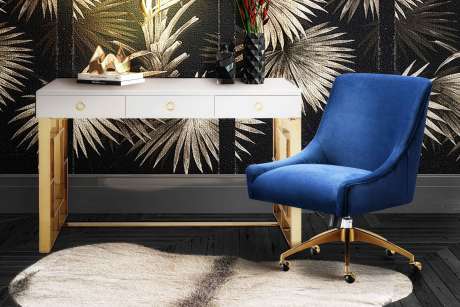 Blue velvet office chair with gold base, white desk with gold legs, and a cowhide rug.

