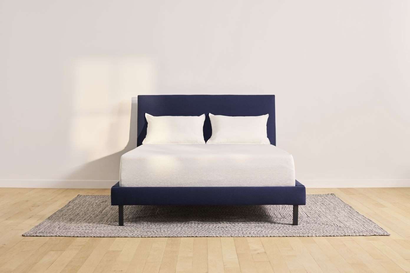 A navy blue bed with two white pillows on a gray rug.
