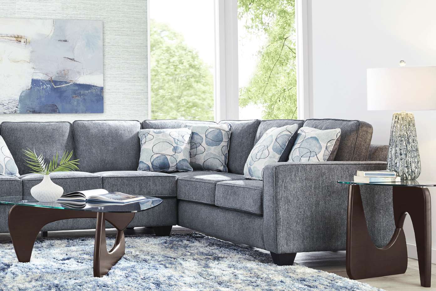 Gray sectional sofa with patterned pillows, glass coffee table, and a rug.