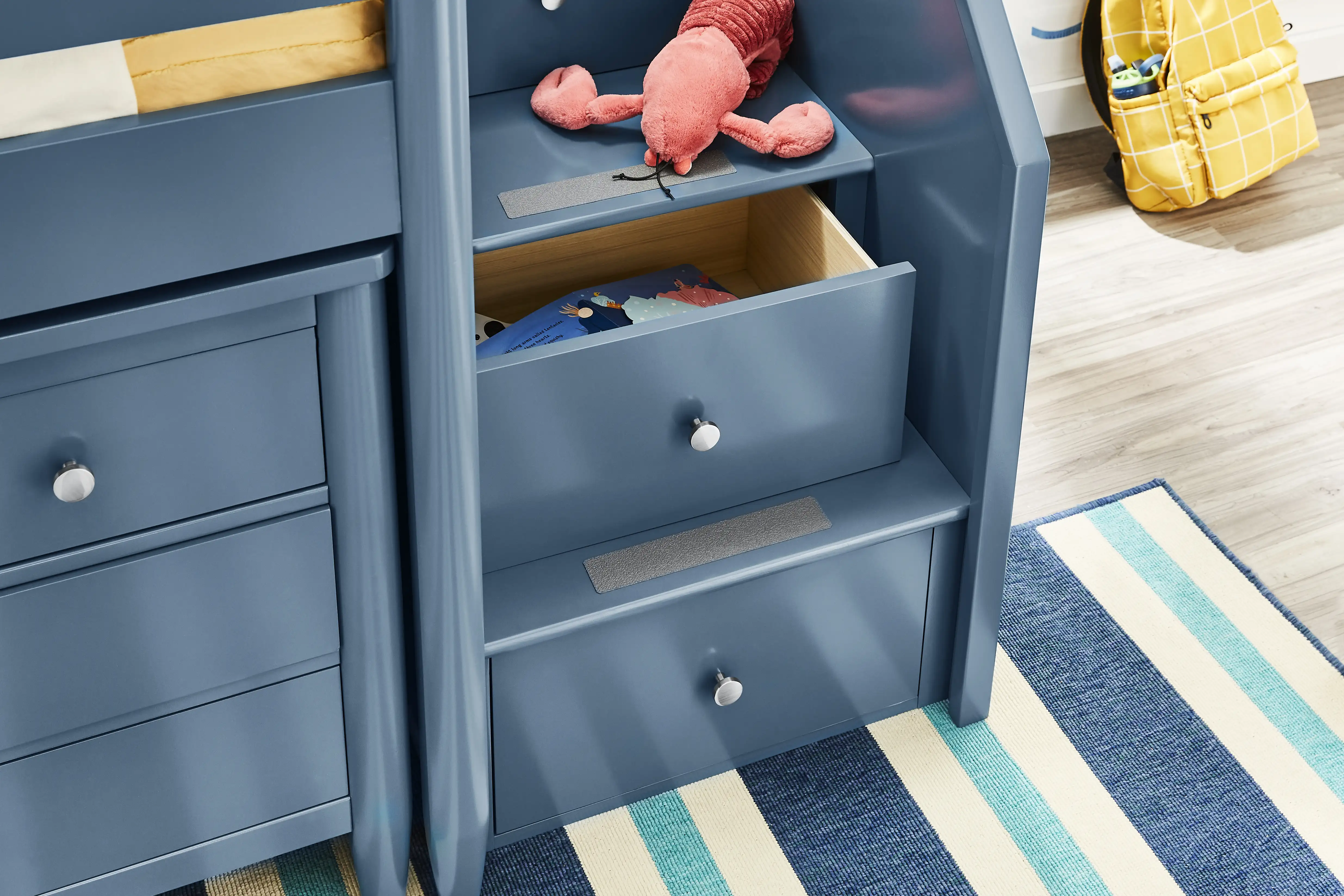 Blue bunk bed with drawers and a lobster plush toy. A yellow backpack is in the background.
