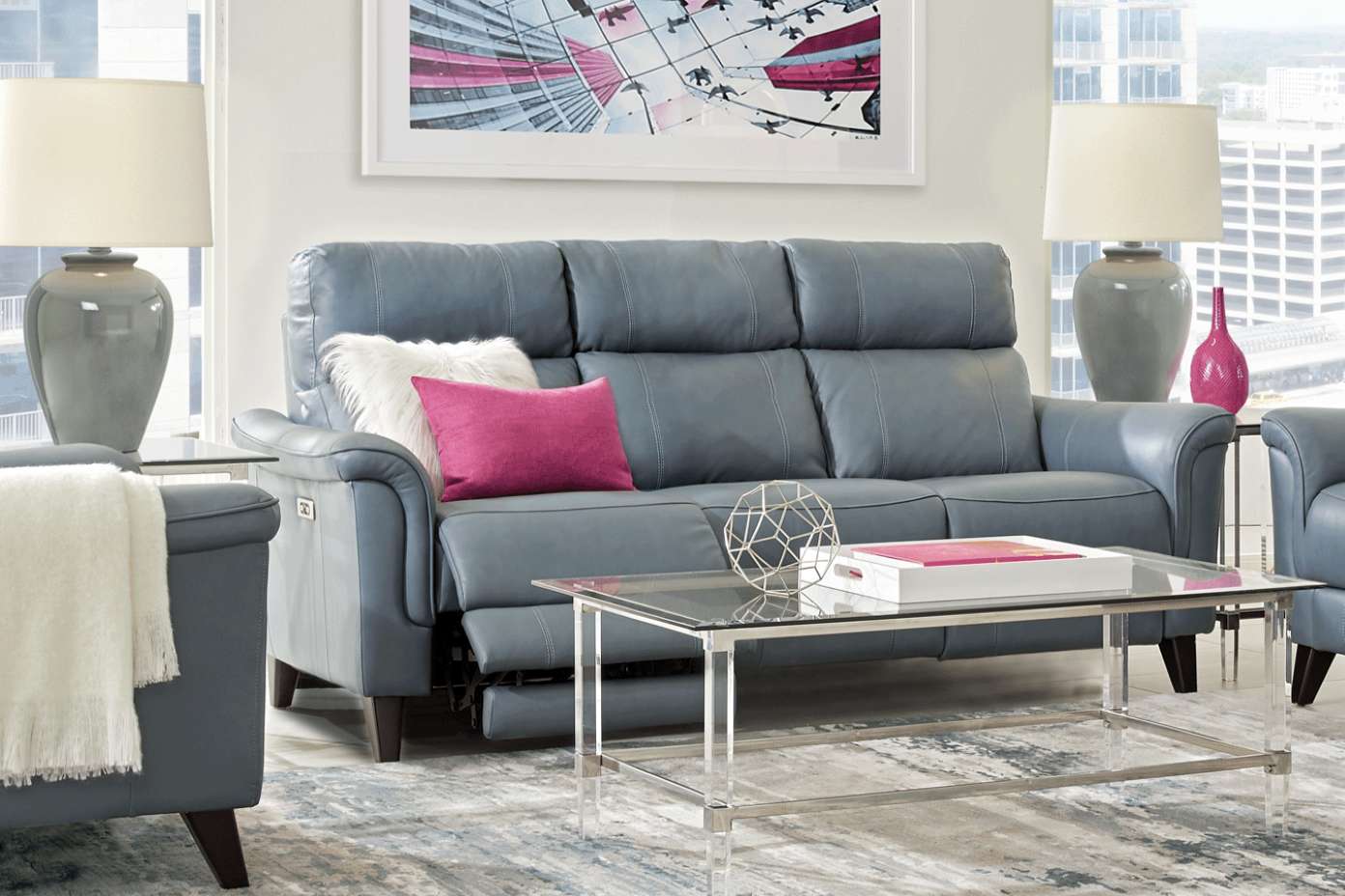 Blue leather sofa with decorative pillows, glass coffee table, and lamps.
