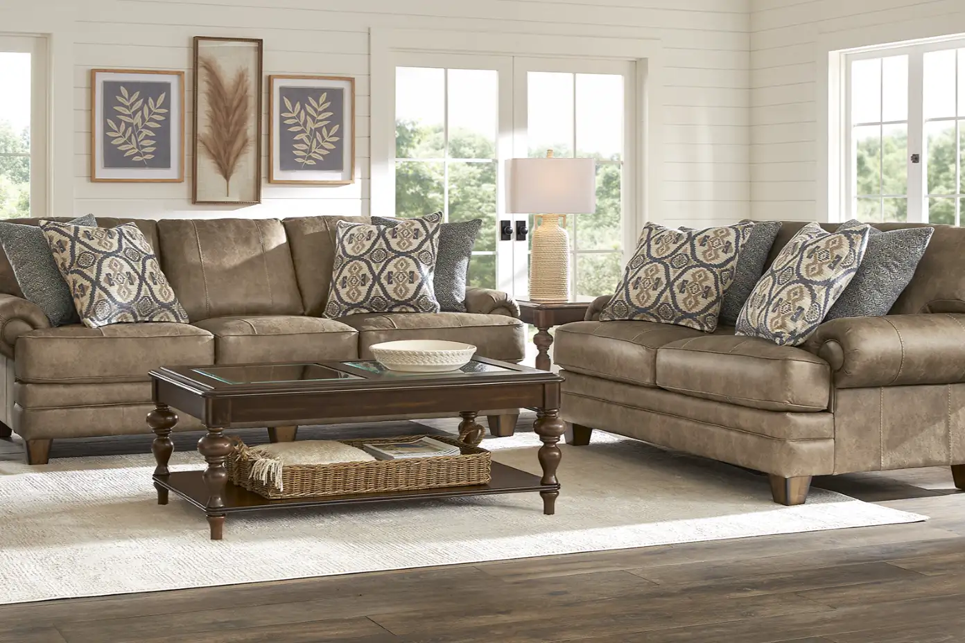 Brown leather sofa and loveseat with patterned pillows, a coffee table, and framed wall art.