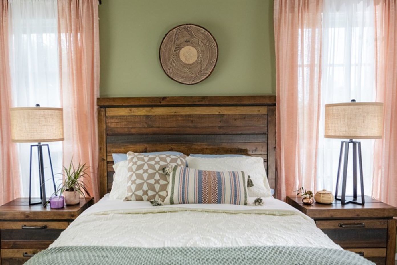 A bedroom with a wooden headboard, lamps, and pink curtains.
