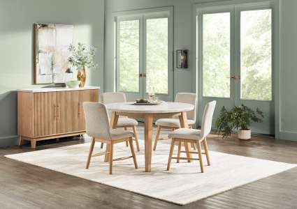 A dining room set with a round table, four chairs, and a sideboard on a rug.
