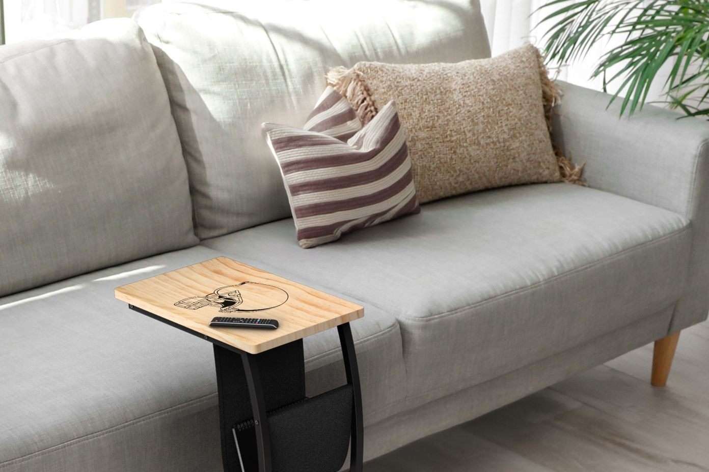 A wooden side table with a football helmet design and a remote on a gray couch.
