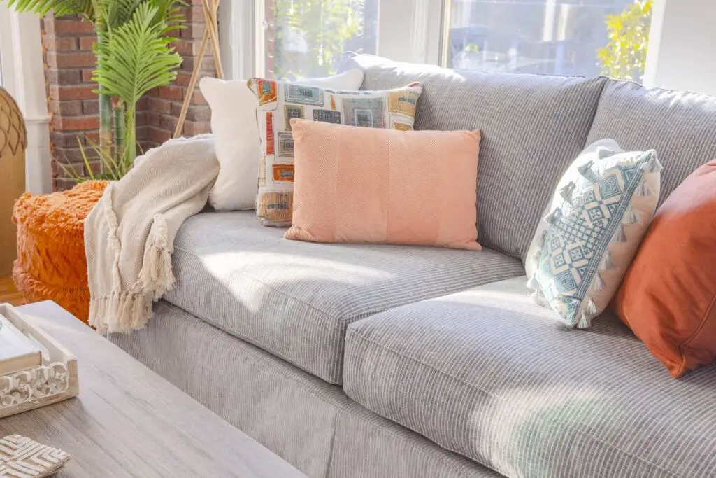 Gray striped sofa with colorful pillows and a throw blanket.
