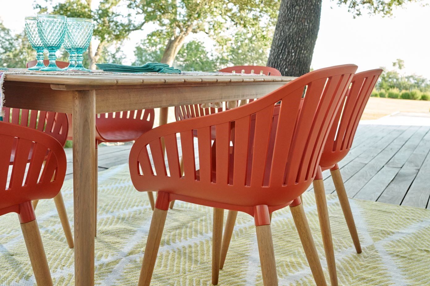 Orange outdoor dining chairs with wooden legs around a wooden table.
