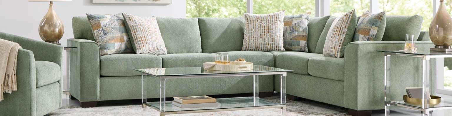 Green sectional sofa with patterned throw pillows and a glass coffee table.