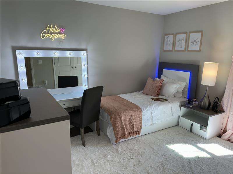 A bedroom with a vanity, bed, and "Hello Gorgeous" neon sign.