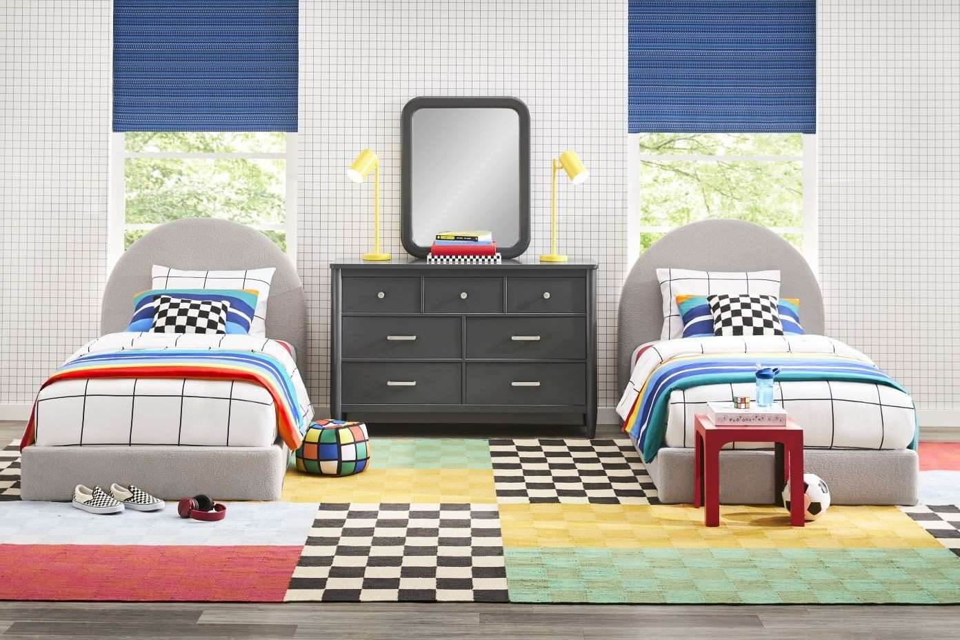 A bedroom with two beds, a dresser, and a colorful rug.