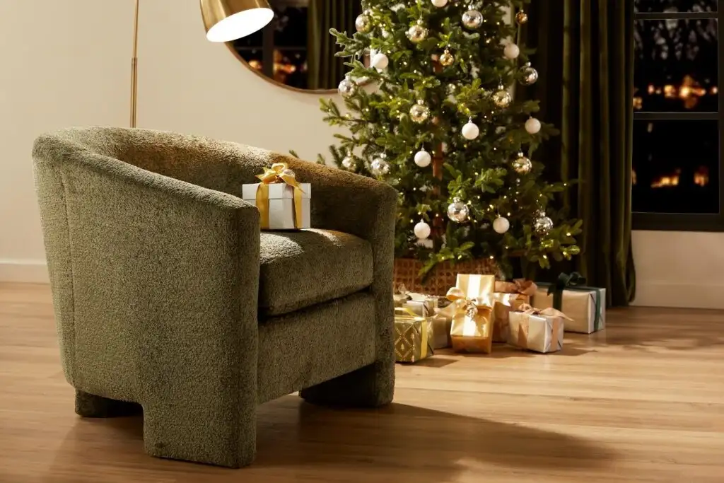 Green armchair with a gift on it, next to a Christmas tree and presents.
