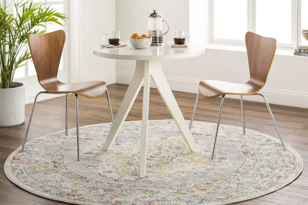 A round white table with two wooden chairs on a patterned rug.