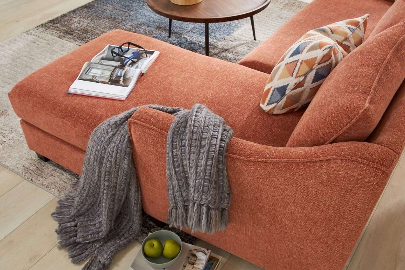 Orange sectional sofa with a gray throw blanket, pillows, and a coffee table.