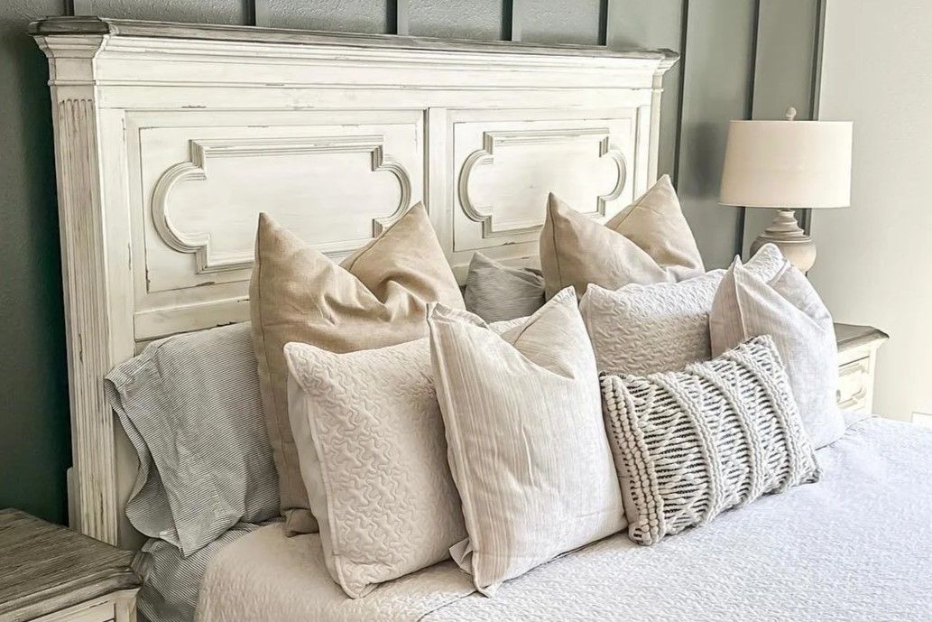 A bed with a white headboard and several pillows.
