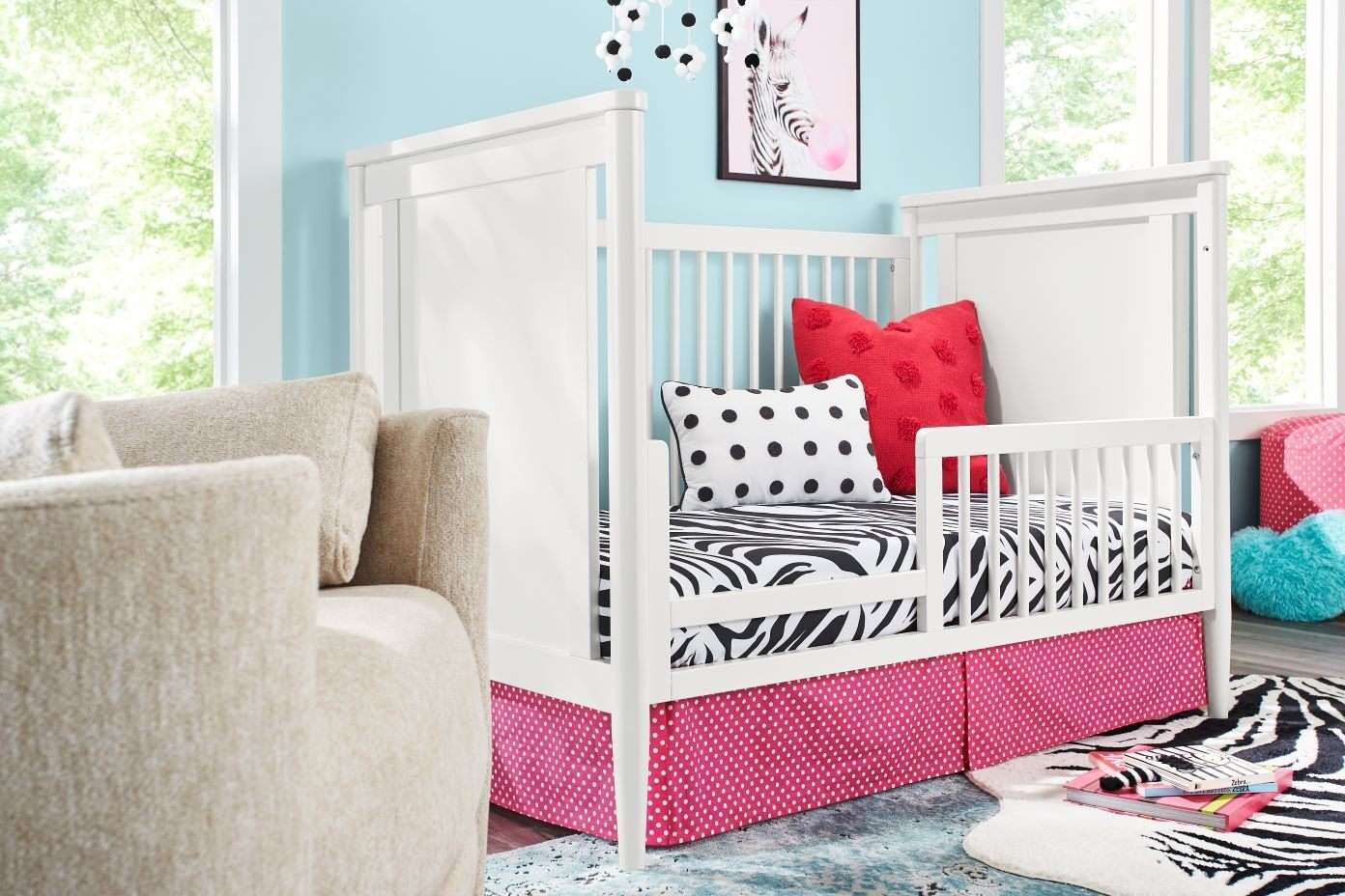White crib with zebra print bedding, red and black polka dot pillows, and a pink polka dot crib skirt.