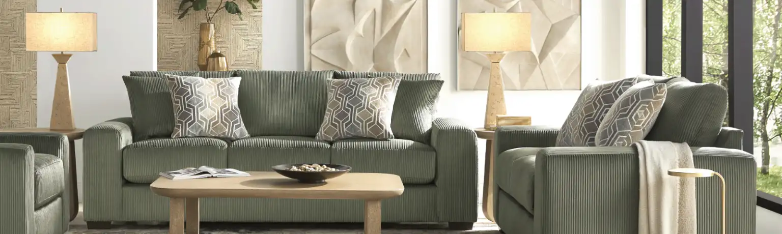 Green corduroy sofa and chairs with patterned pillows, lamps, and a wooden coffee table.