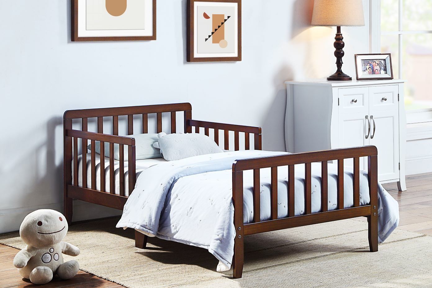 Brown toddler bed with a white comforter and a stuffed animal.
