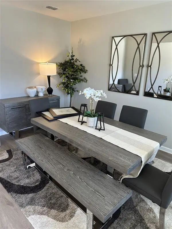 A dining room with a gray wooden table, bench, and chairs, a rug, and decorative mirrors.
