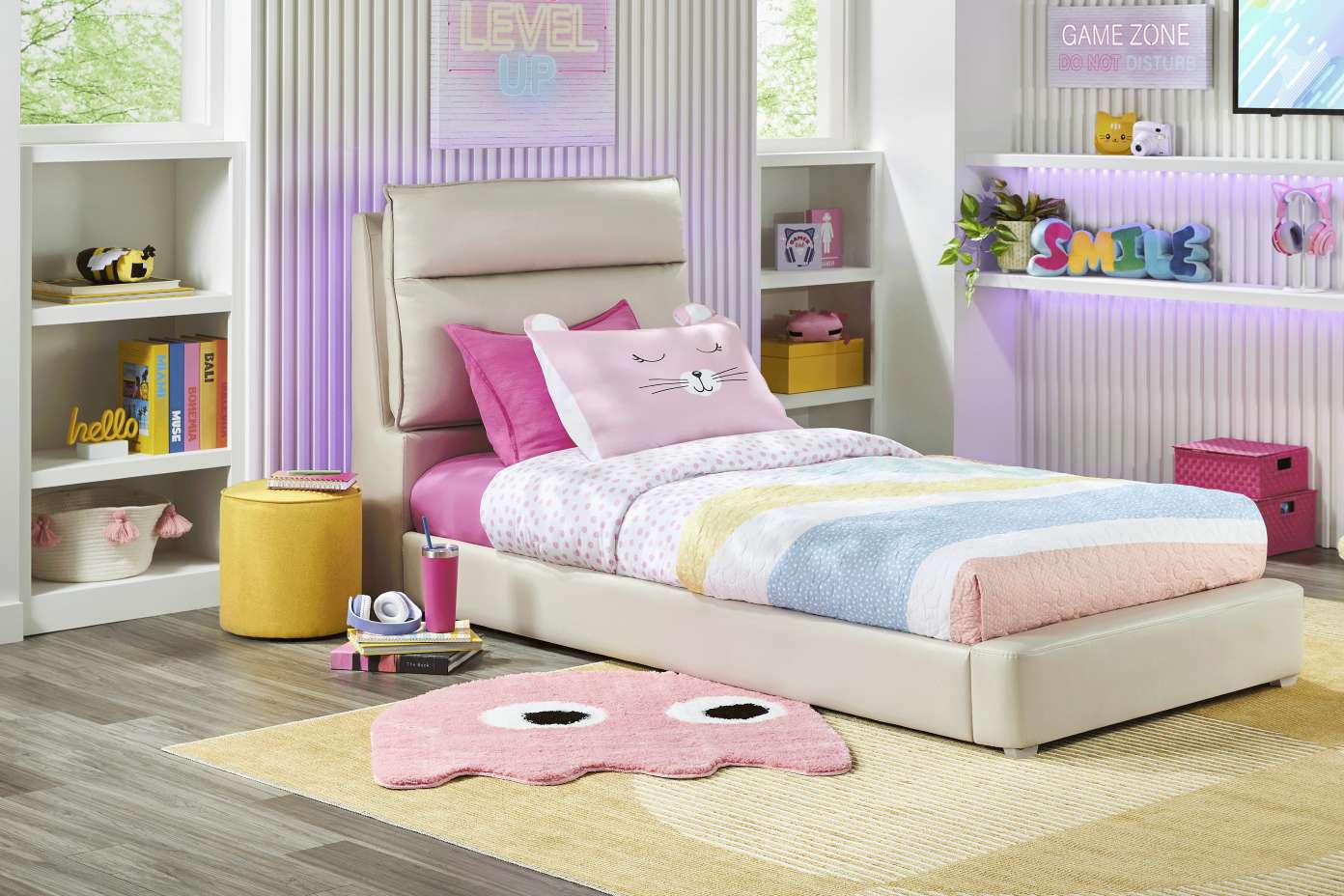 A bedroom with a bed, shelves, and a rug. The bed has a pink cat pillow and a colorful comforter.
