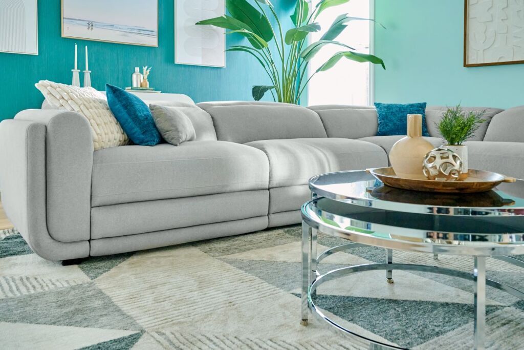 A light gray sectional sofa with blue and white pillows, a round coffee table, and a patterned rug.
