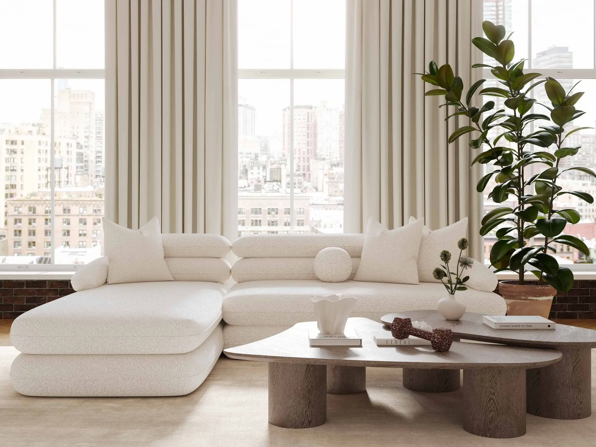 A modern, cream-colored sectional sofa with a chaise, paired with a wooden coffee table in a bright, city-view living room.