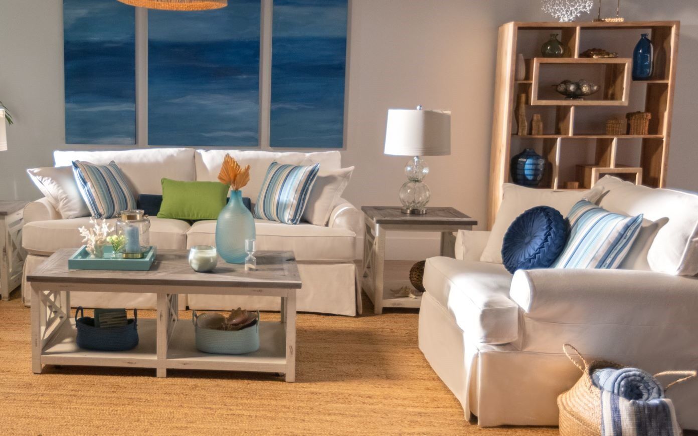 Living room with white sofas, blue and green pillows, and a wooden bookshelf.
