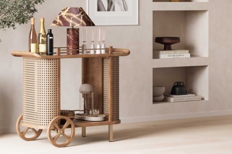 A wooden bar cart with a lamp, bottles, and glasses.
